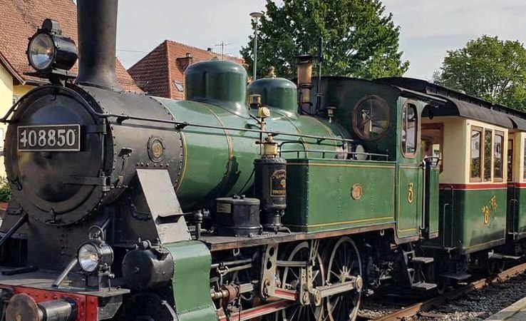 Eine grüne historische Dampflokomotive steht auf einem Gleis in Nürtingen. Der Himmel ist leicht bewölkt, und im Hintergrund sind Bäume und Häuser zu sehen., © StadtNürtingen Eine grüne historische Dampflokomotive steht auf einem Gleis in Nürtingen. Der Himmel ist leicht bewölkt, und im Hintergrund sind Bäume und Häuser zu sehen., © StadtNürtingen
