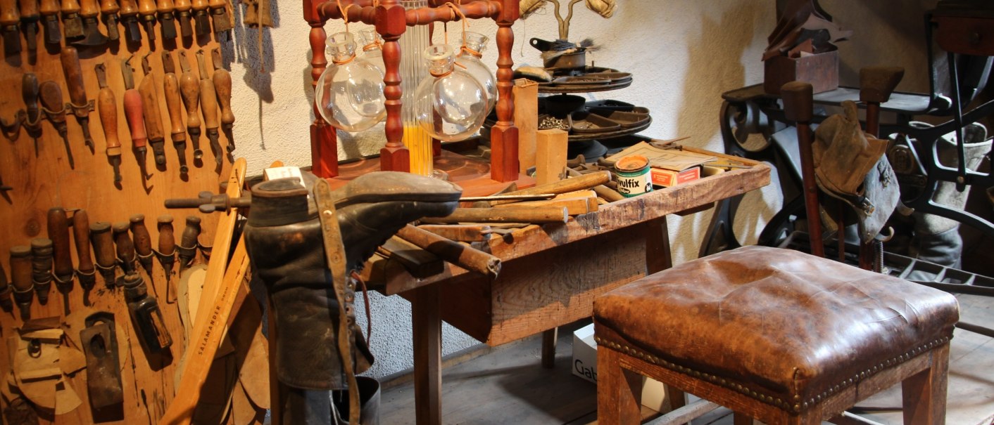 Eine alte Werkstatt im Flößermuseum Calmbach mit Werkzeugen, Lederstiefel und einem Holzhocker. An der Wand hängen zahlreiche Handwerkzeuge., © Touristik Bad Wildbad GmbH Eine alte Werkstatt im Flößermuseum Calmbach mit Werkzeugen, Lederstiefel und einem Holzhocker. An der Wand hängen zahlreiche Handwerkzeuge., © Touristik Bad Wildbad GmbH