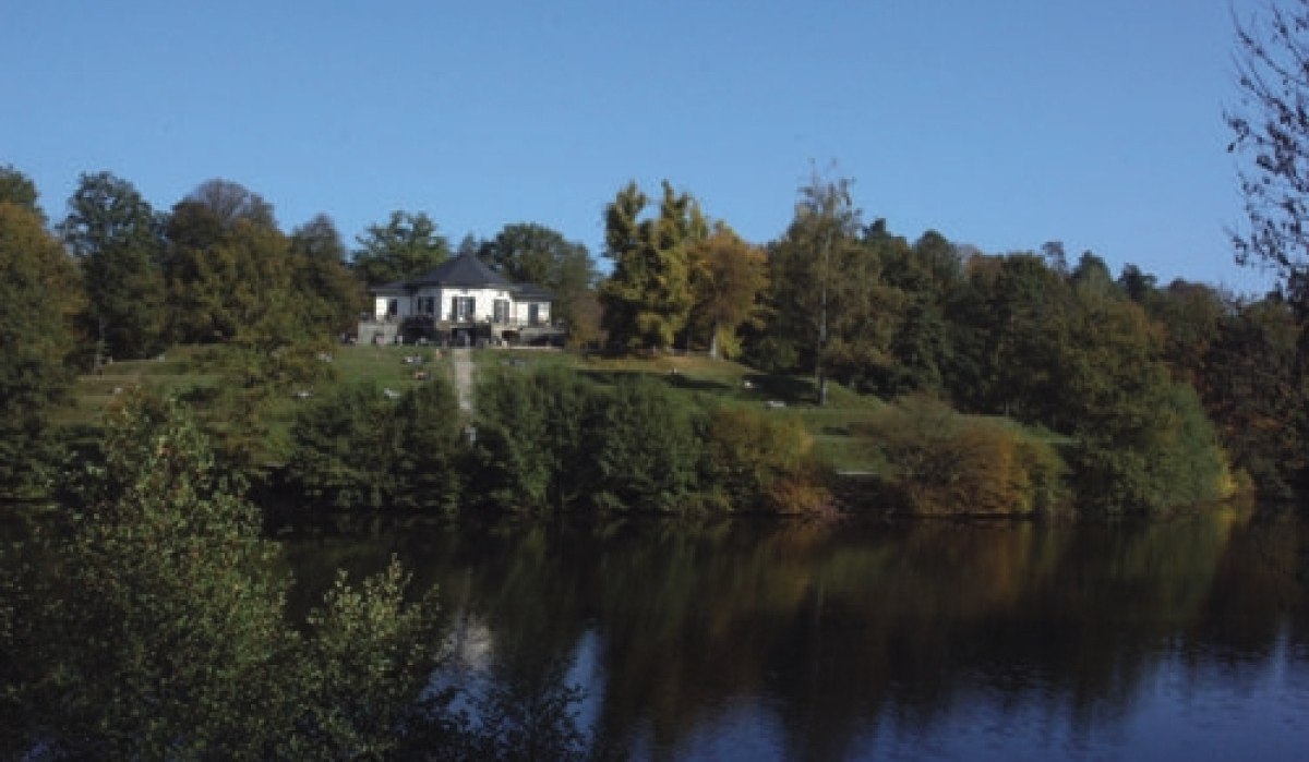 Das Bärenschlössle steht auf einem Hügel, umgeben von Bäumen, mit einem See im Vordergrund unter klarem, blauem Himmel., © Sindelfingen - Stuttgart-Marketing GmbH Das Bärenschlössle steht auf einem Hügel, umgeben von Bäumen, mit einem See im Vordergrund unter klarem, blauem Himmel., © Sindelfingen - Stuttgart-Marketing GmbH