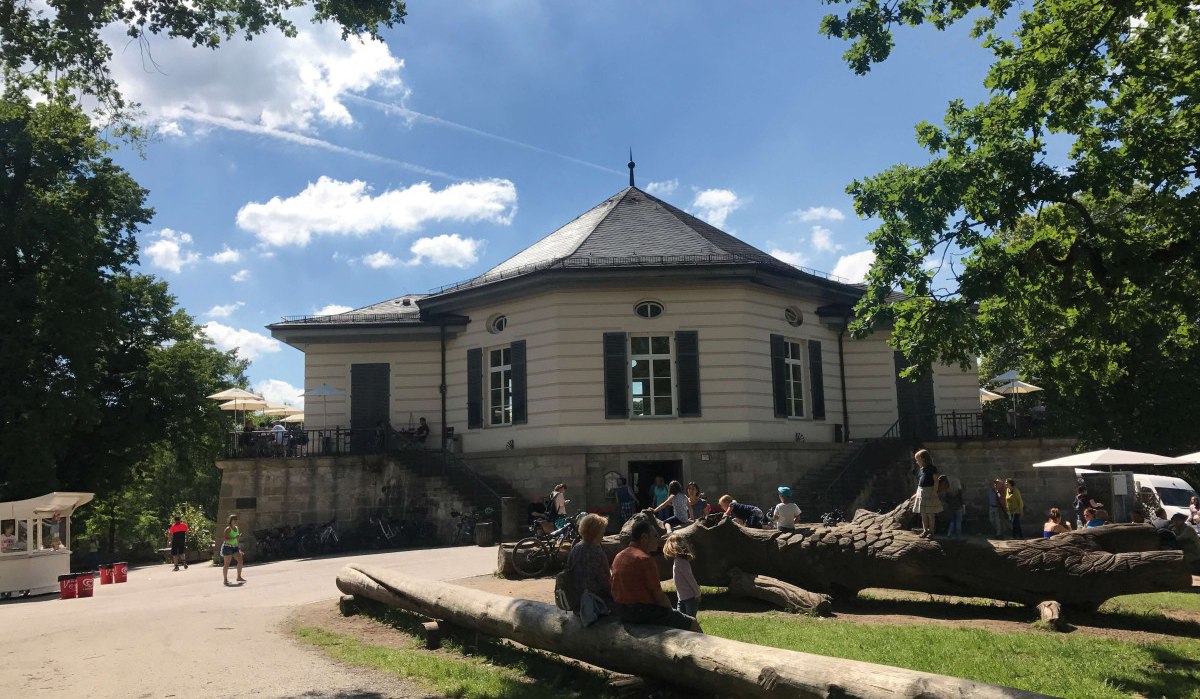 Das Bärenschlössle in einem sonnigen Park. Menschen sitzen und spielen auf Baumstämmen, während andere spazieren gehen. Der Himmel ist blau mit Wolken., © Stuttgart-Marketing GmbH Das Bärenschlössle in einem sonnigen Park. Menschen sitzen und spielen auf Baumstämmen, während andere spazieren gehen. Der Himmel ist blau mit Wolken., © Stuttgart-Marketing GmbH
