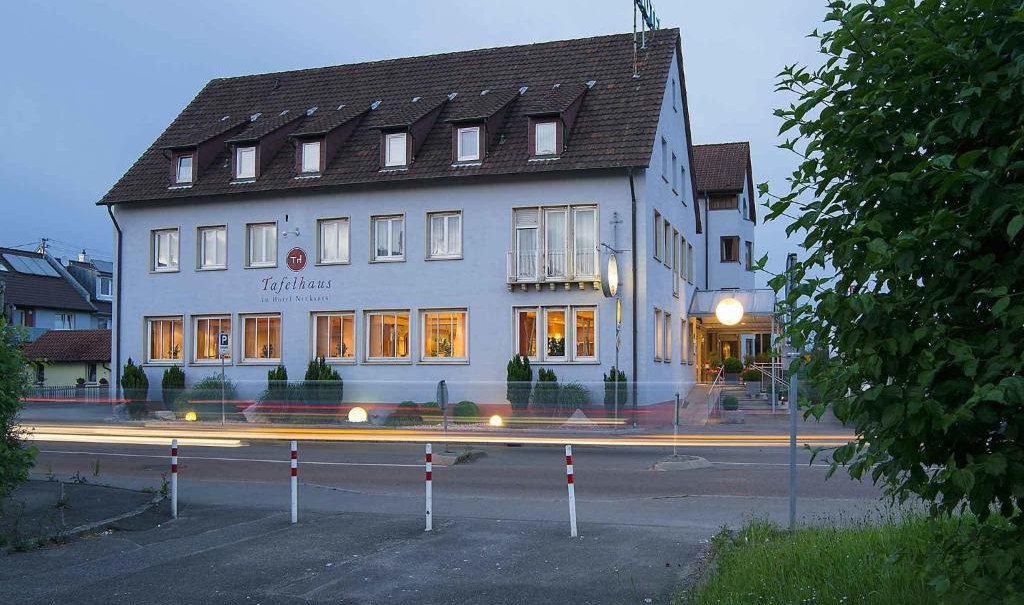 Ein Hotel mit beleuchteten Fenstern bei Dämmerung. Autos fahren vorbei, was Lichtspuren erzeugt. Das Gebäude hat ein Satteldach und mehrere Etagen., © Nödinger Gastro GmbH