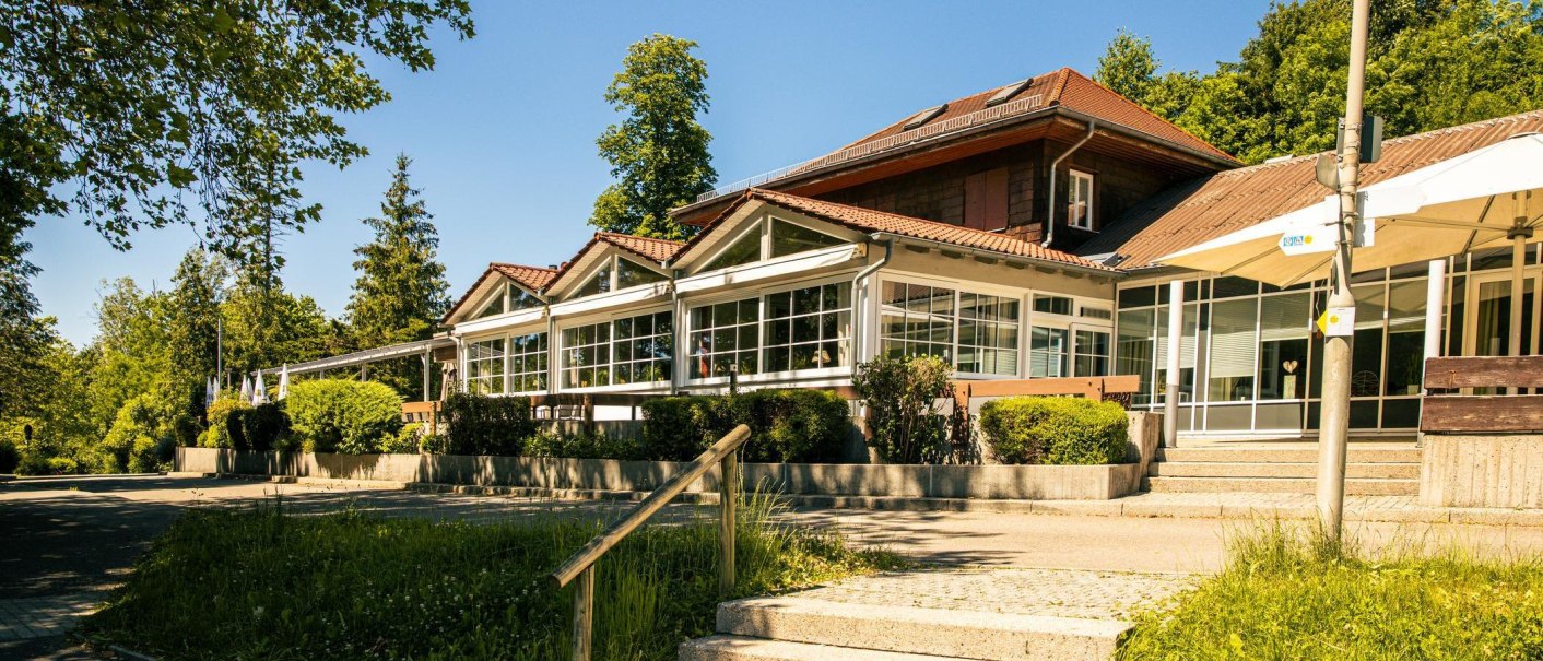 Ein modernes Gebäude mit großen Fenstern und rotem Dach, umgeben von Bäumen und Grünflächen. Der Himmel ist klar und blau., © Stuttgart-Marketing GmbH, Sarah Schmid Ein modernes Gebäude mit großen Fenstern und rotem Dach, umgeben von Bäumen und Grünflächen. Der Himmel ist klar und blau., © Stuttgart-Marketing GmbH, Sarah Schmid