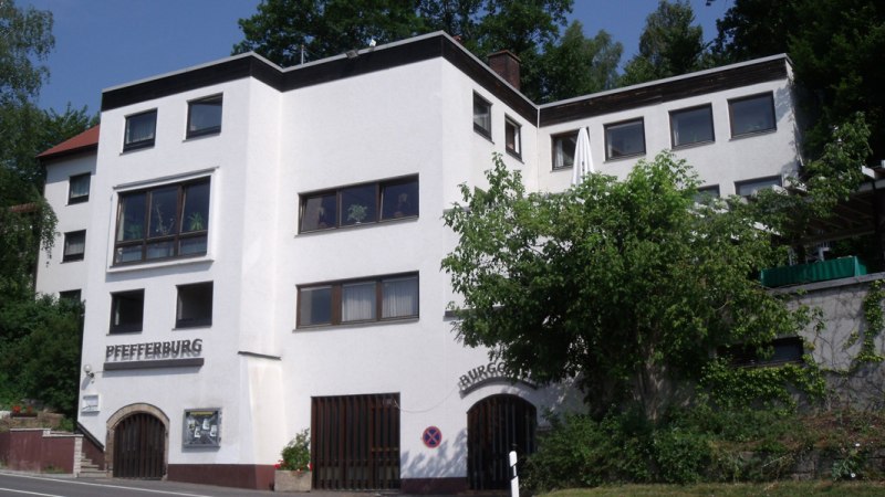 Das Hotel Pfefferburg hat eine weiße Fassade mit großen Fenstern und ist von Bäumen umgeben. Der Schriftzug 'Pfefferburg' ist gut sichtbar., © Landgasthof Hotel Pfefferburg