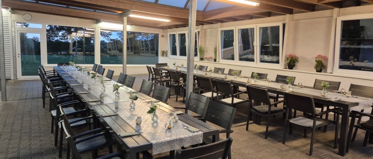 Ein überdachter Außenbereich mit langen, gedeckten Tischen und Stühlen, dekoriert mit kleinen Blumenvasen. Die Umgebung wirkt einladend und modern., © Restaurant Lingam Ein überdachter Außenbereich mit langen, gedeckten Tischen und Stühlen, dekoriert mit kleinen Blumenvasen. Die Umgebung wirkt einladend und modern., © Restaurant Lingam