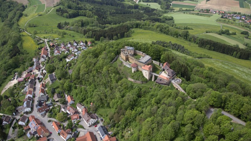 Luftaufnahme der Burgruine Rechberg in Schwäbisch Gmünd, umgeben von grünen Wäldern und einem kleinen Dorf. Felder und Wälder erstrecken sich im Hintergrund., © Burg Rechberg