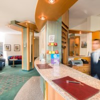 Hotelrezeption mit geschwungener Theke, Dekoration mit Äpfeln und Eule, sowie einem verschwommenen Mitarbeiter im Anzug. Sitzbereich im Hintergrund., © Plaza Hotel Blankenburg Ditzingen Hotelrezeption mit geschwungener Theke, Dekoration mit Äpfeln und Eule, sowie einem verschwommenen Mitarbeiter im Anzug. Sitzbereich im Hintergrund., © Plaza Hotel Blankenburg Ditzingen