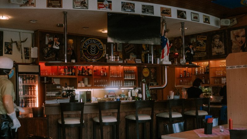 Gem&uuml;tliche Bar mit Holzm&ouml;beln, Flaggen an der Decke und dekorativen Postern. Die Theke ist gut best&uuml;ckt, und es gibt mehrere Sitzm&ouml;glichkeiten., &copy; Archie