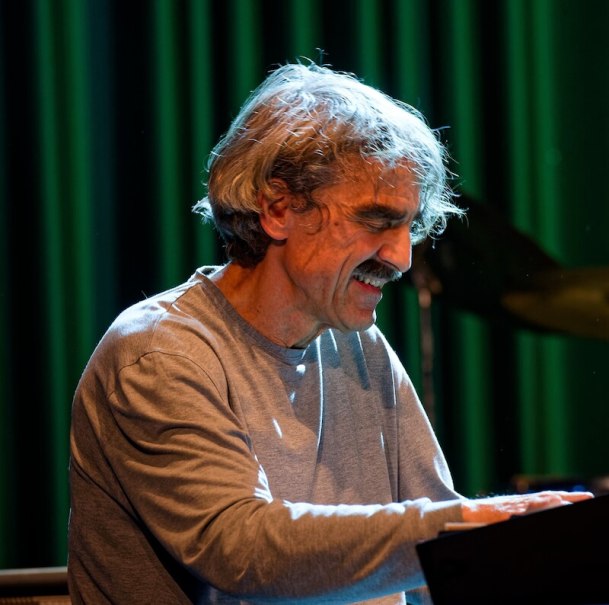 Ein Mann spielt Klavier auf einer Bühne. Er trägt ein graues Shirt und wirkt konzentriert. Der Hintergrund ist grün beleuchtet., © Thomas Scheytt Ein Mann spielt Klavier auf einer Bühne. Er trägt ein graues Shirt und wirkt konzentriert. Der Hintergrund ist grün beleuchtet., © Thomas Scheytt