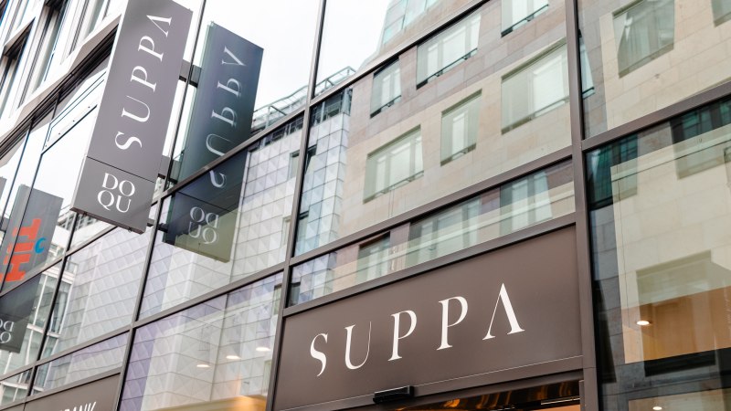 Glasfassade eines modernen Gebäudes mit mehreren SUPPA-Schildern. Die Spiegelung zeigt umliegende Architektur., © SMG_Sarah Schmid