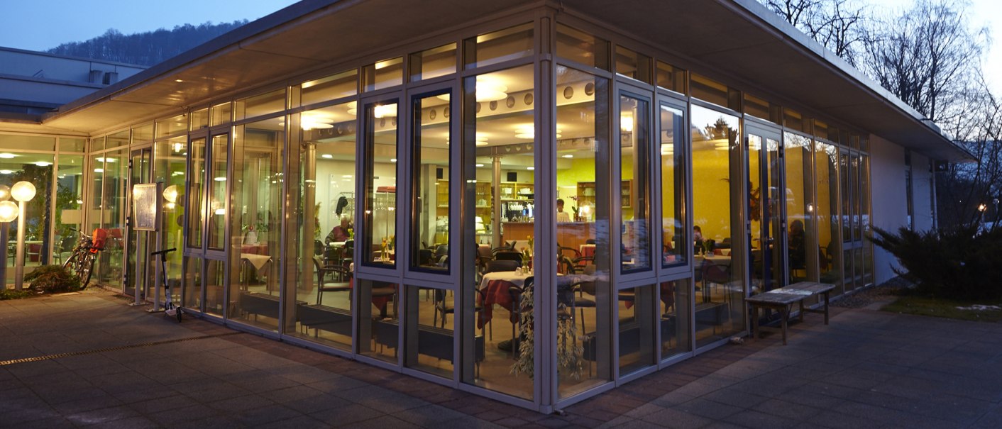 Modernes Café mit Glaswänden, beleuchtet in der Dämmerung. Innen sind Tische und Stühle sichtbar, draußen stehen ein Fahrrad und ein Roller., © Vinzenz Therme Bad Ditzenbach / Peter Flämig Modernes Café mit Glaswänden, beleuchtet in der Dämmerung. Innen sind Tische und Stühle sichtbar, draußen stehen ein Fahrrad und ein Roller., © Vinzenz Therme Bad Ditzenbach / Peter Flämig