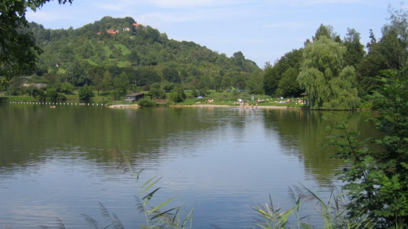 Ein See mit ruhigem Wasser, umgeben von gr&uuml;nen H&uuml;geln und B&auml;umen. Menschen entspannen am Ufer., &copy; Remstal Tourismus e.V.