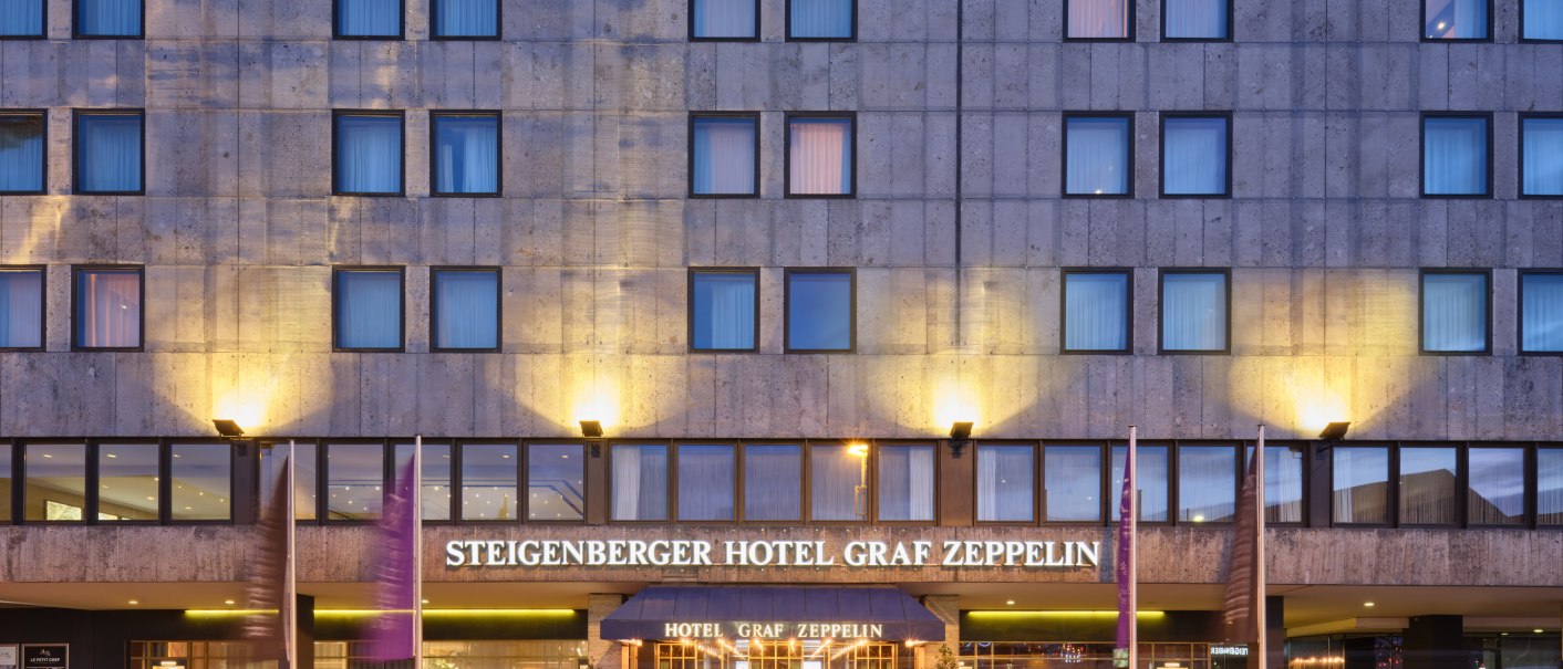 Das Steigenberger Hotel Graf Zeppelin bei Dämmerung. Die Fassade ist beleuchtet, und Lichtspuren von Autos sind auf der Straße sichtbar., © Steigenberger Graf Zeppelin