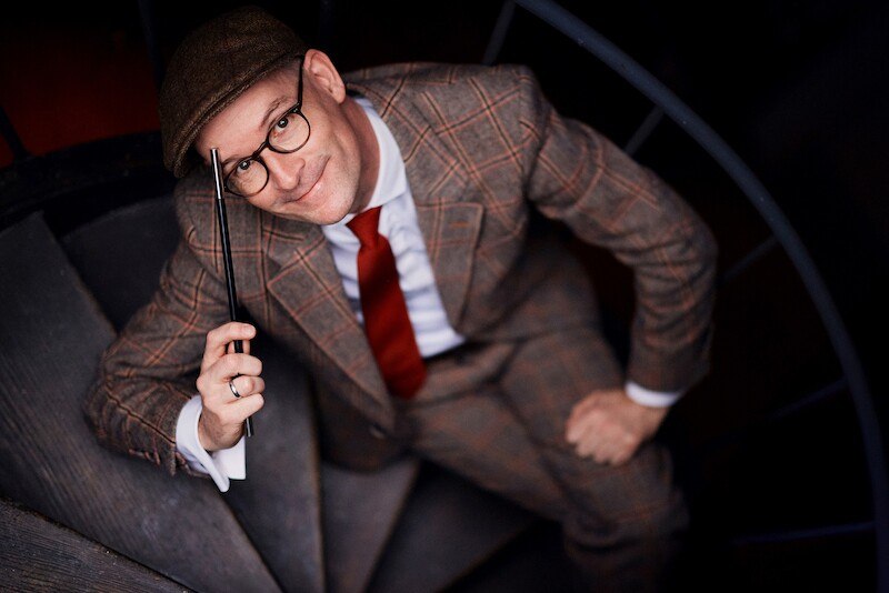 Mann in kariertem Anzug und roter Krawatte auf einer Wendeltreppe, hält einen Zauberstab., © Kulturhaus Schwanen