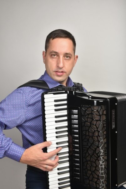 Ein Mann in einem blauen Hemd spielt Akkordeon vor einem neutralen Hintergrund. Er schaut direkt in die Kamera., © Roman Dotsenko Ein Mann in einem blauen Hemd spielt Akkordeon vor einem neutralen Hintergrund. Er schaut direkt in die Kamera., © Roman Dotsenko