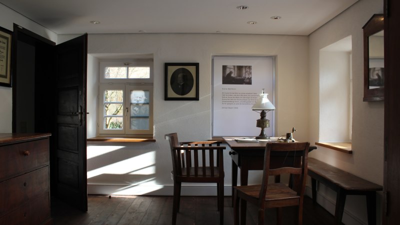 Historisches Zimmer im Christian-Wagner-Haus mit Holztisch, Stühlen, Lampe und Fenster. Bilder und Texte an den Wänden., © Stadt Leonberg Historisches Zimmer im Christian-Wagner-Haus mit Holztisch, Stühlen, Lampe und Fenster. Bilder und Texte an den Wänden., © Stadt Leonberg