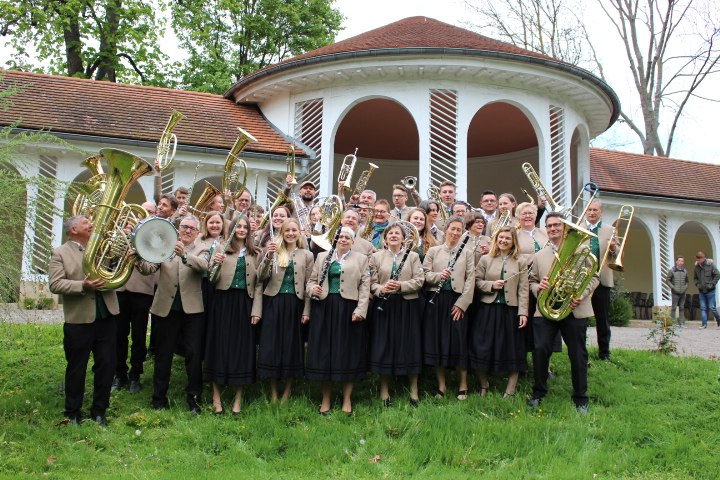Eine Blaskapelle in traditioneller Kleidung steht vor einem runden Gebäude mit Bögen und rotem Dach., © Musikverein Bad Boll Eine Blaskapelle in traditioneller Kleidung steht vor einem runden Gebäude mit Bögen und rotem Dach., © Musikverein Bad Boll