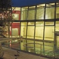 Modernes Gebäude mit Glasfassade, beleuchtet bei Nacht. Ein kleiner Pool oder Wasserfläche spiegelt das Licht wider. Bäume im Vordergrund., © Schwäbische Alb