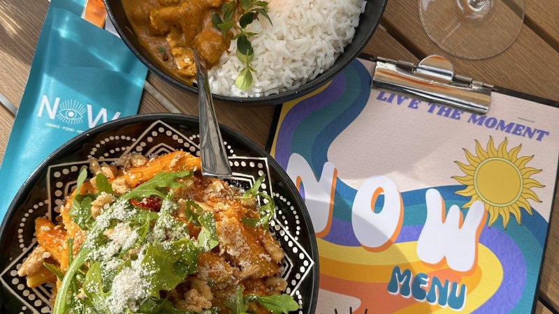 Ein Tisch mit Curry und Reis, Pasta mit Rucola, einem Getr&auml;nk und einer bunten Speisekarte mit der Aufschrift 'NOW'., &copy; NOW