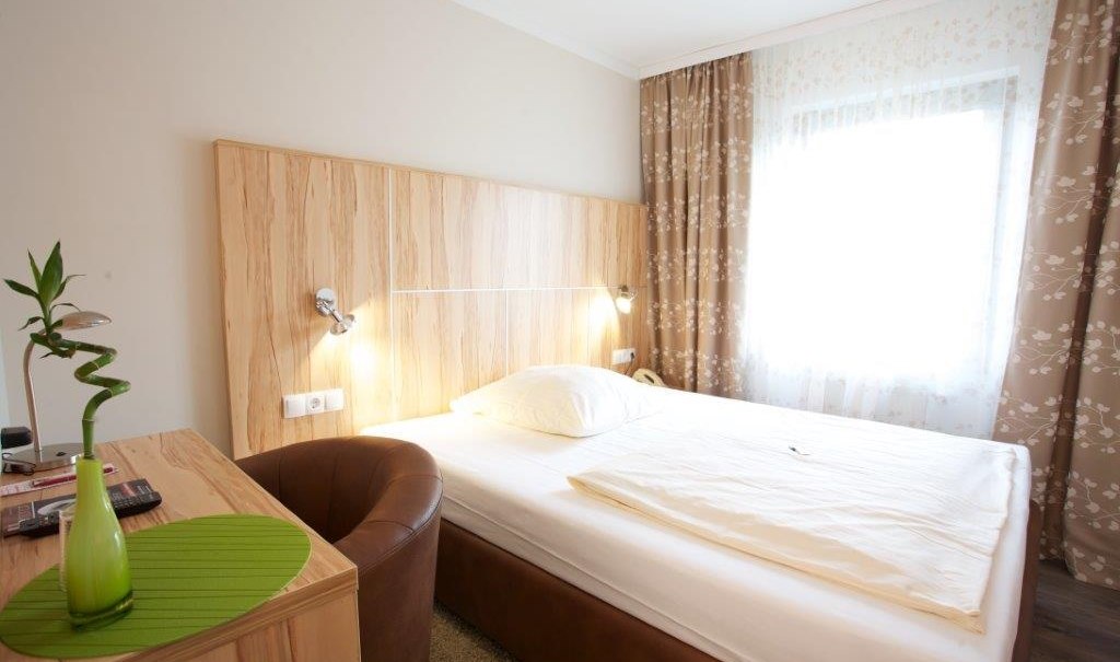 Ein gemütliches Einzelzimmer mit einem Bett, einem Schreibtisch, einem Sessel und einem Fenster mit gemusterten Vorhängen., © Hotel Reinhardtshof Garni