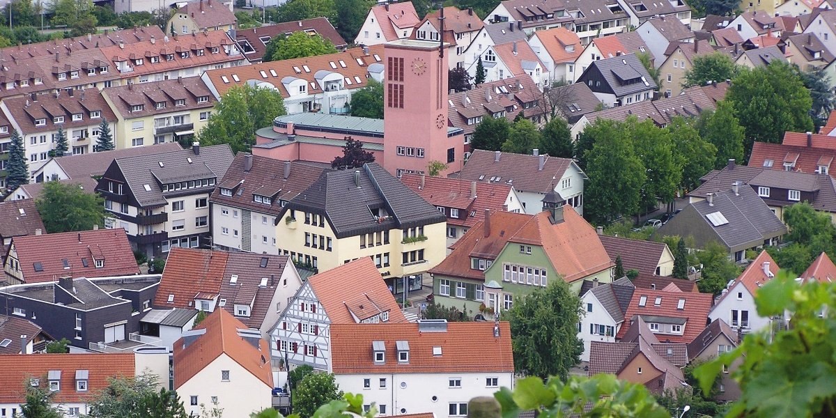 Luftaufnahme von Hedelfingen: Eine Kirche mit Turm in der Mitte, umgeben von dicht stehenden Wohnh&auml;usern mit roten D&auml;chern und gr&uuml;nen B&auml;umen., &copy; Stuttgart-Marketing GmbH
