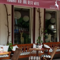 Gemütlicher Außenbereich des Restaurant Café Hirsch mit Holzbänken, Tischen und Pflanzen. Ein rotes Vordach mit Schriftzug ist sichtbar., © Restaurant Café Hirsch
