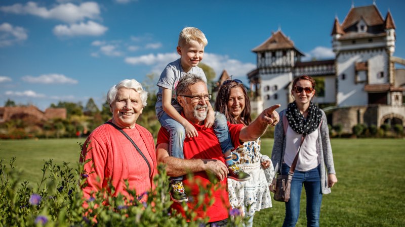 Eine fr&ouml;hliche Familie posiert in einem Garten vor einem Schloss. Ein &auml;lterer Mann tr&auml;gt ein Kind auf den Schultern und zeigt in die Ferne., &copy; Erlebnispark Tripsdrill