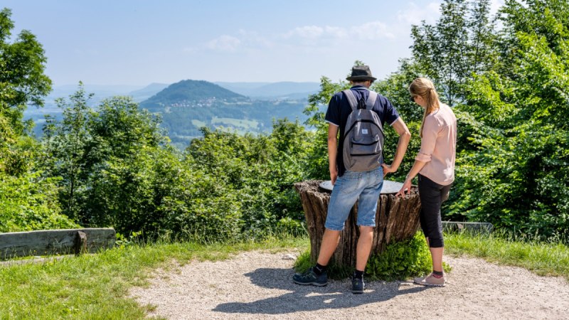 Zwei Personen betrachten von einem Aussichtspunkt aus die Landschaft mit einem bewaldeten Hügel im Hintergrund., © TMBW, Gregor Lengler
