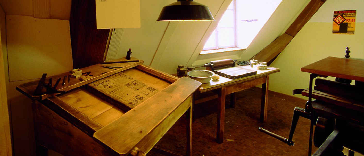 Historische Druckwerkstatt im J.-F.-Schreiber Museum Esslingen mit Holztischen, Druckutensilien und einem Fenster im Hintergrund., © Esslinger Stadtmarketing & Tourismus GmbH