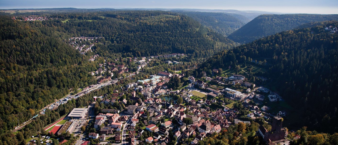 Luftaufnahme von Bad Liebenzell im Schwarzwald, umgeben von dichten Wäldern und Hügeln. Die Stadt liegt in einem Tal mit vielen Gebäuden und Straßen., © Stuttgart-Marketing GmbH