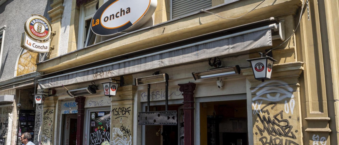 Fassade einer Bar namens La Concha mit Graffiti und Schildern von Erdinger Weißbräu. Die Außenwände sind mit Graffiti verziert., © SMG, Sarah Schmid