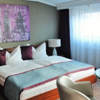 Komfortables Doppelzimmer mit großem Bett, zwei Nachttischen, Tisch und Stühlen. Helle Vorhänge und moderne Dekoration an der Wand., © Hotel Pelikan Komfortables Doppelzimmer mit großem Bett, zwei Nachttischen, Tisch und Stühlen. Helle Vorhänge und moderne Dekoration an der Wand., © Hotel Pelikan