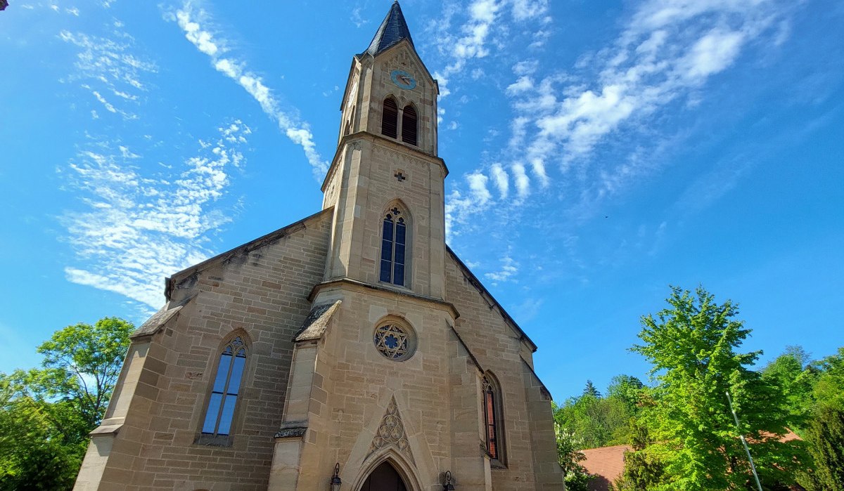 Die Evangelische Schlosskirche Remseck-Hochberg vor blauem Himmel mit dekorativen Wolken. Der Kirchturm ragt in die Höhe, umgeben von Bäumen. Die Evangelische Schlosskirche Remseck-Hochberg vor blauem Himmel mit dekorativen Wolken. Der Kirchturm ragt in die Höhe, umgeben von Bäumen.