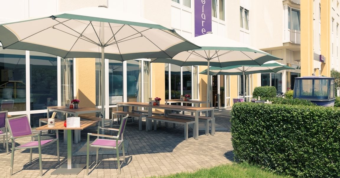 Terrasse mit Holztischen, lila Stühlen und großen Sonnenschirmen vor einem gelben Gebäude mit großen Fenstern., © Mercure Hotel Stuttgart Gerlingen Terrasse mit Holztischen, lila Stühlen und großen Sonnenschirmen vor einem gelben Gebäude mit großen Fenstern., © Mercure Hotel Stuttgart Gerlingen