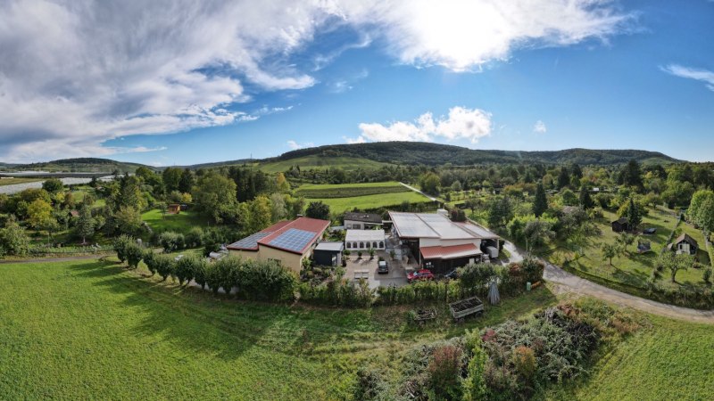 Luftaufnahme des Weinguts Ei&szlig;ele mit Geb&auml;uden, Feldern und B&auml;umen. Im Hintergrund H&uuml;gel und blauer Himmel mit Wolken., &copy; Weingut Ei&szlig;ele