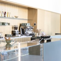Modernes Café mit glänzender Theke, Kaffeemaschine und Regalen mit Tassen und Flaschen an der Wand., © Dominique Brewing Modernes Café mit glänzender Theke, Kaffeemaschine und Regalen mit Tassen und Flaschen an der Wand., © Dominique Brewing