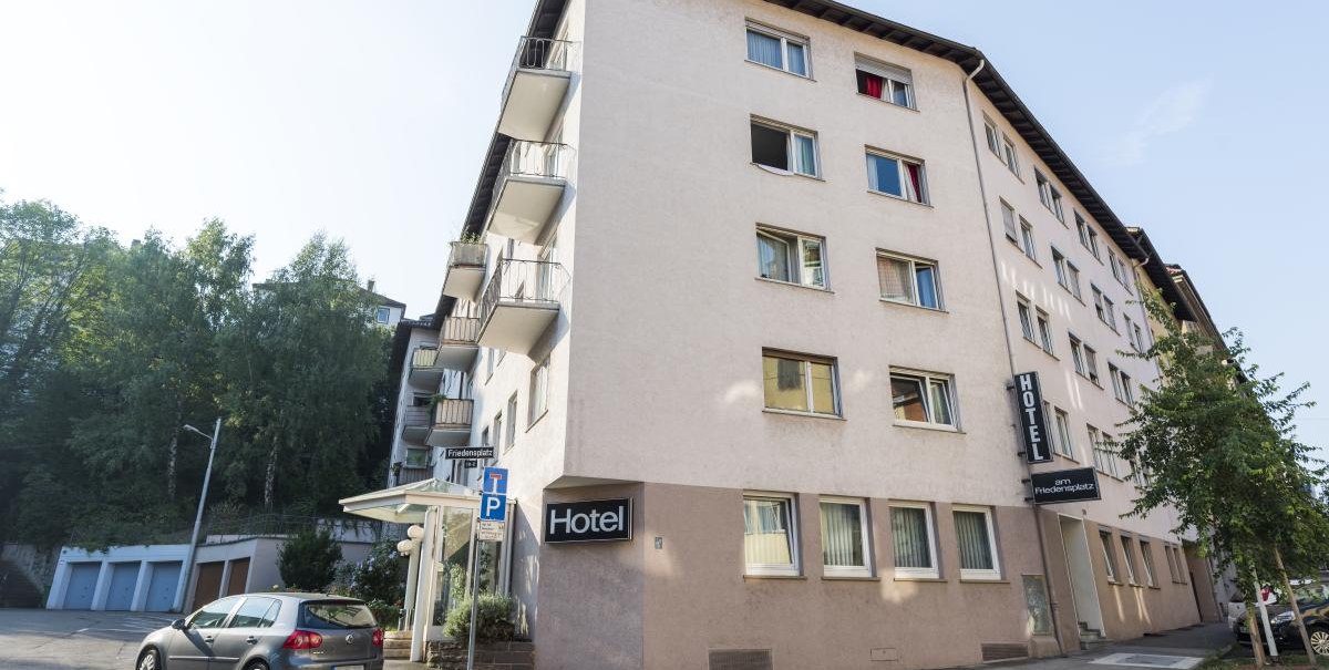Mehrstöckiges Hotel mit Balkonen, geparktes Auto davor, Straßenschild 'Friedensplatz' sichtbar. Klare, sonnige Wetterbedingungen., © ARNOTEL GmbH Mehrstöckiges Hotel mit Balkonen, geparktes Auto davor, Straßenschild 'Friedensplatz' sichtbar. Klare, sonnige Wetterbedingungen., © ARNOTEL GmbH