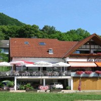 Café Köhler mit Terrasse und Sonnenschirmen, umgeben von grüner Landschaft und einem bewaldeten Hügel im Hintergrund., © Café Köhler Café Köhler mit Terrasse und Sonnenschirmen, umgeben von grüner Landschaft und einem bewaldeten Hügel im Hintergrund., © Café Köhler
