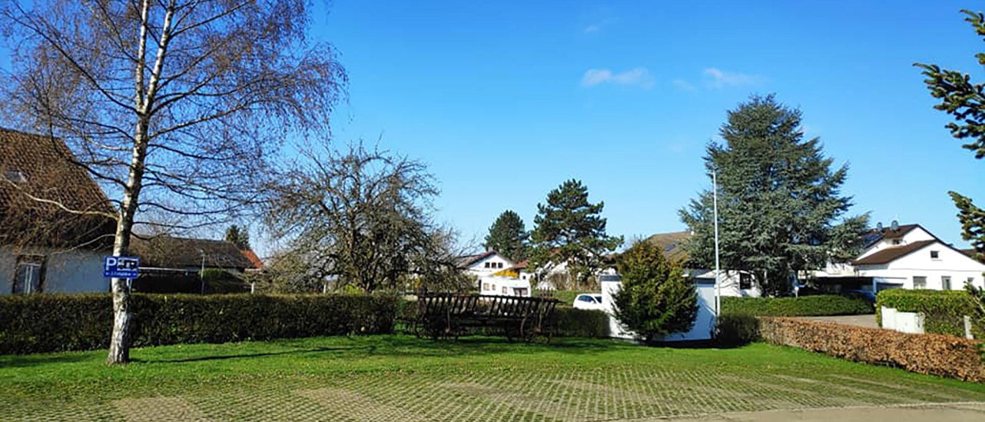 Ein Wohnmobilstellplatz mit Bäumen und einem Parkplatzschild. Im Hintergrund sind Häuser und ein blauer Himmel zu sehen., © Dieter Schurr, Gasthaus Hirsch