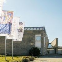 Das Museum Im Kleinhues-Bau in Kornwestheim, moderne Architektur mit mehreren Fahnen im Vordergrund, sonniger Tag., © SMG, Sarah Schmid Das Museum Im Kleinhues-Bau in Kornwestheim, moderne Architektur mit mehreren Fahnen im Vordergrund, sonniger Tag., © SMG, Sarah Schmid