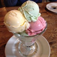 Ein Glasbecher mit drei Kugeln Eis in den Farben Gelb, Grün und Rosa steht auf einem Holztisch., © StadtNürtingen Ein Glasbecher mit drei Kugeln Eis in den Farben Gelb, Grün und Rosa steht auf einem Holztisch., © StadtNürtingen