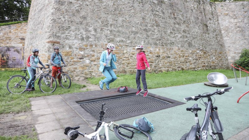 Zwei Personen springen auf einem Trampolin neben Fahrrädern vor einer alten Steinmauer. Weitere Personen stehen mit Fahrrädern daneben., © Schwäbische Alb Tourismusverband e.V. Zwei Personen springen auf einem Trampolin neben Fahrrädern vor einer alten Steinmauer. Weitere Personen stehen mit Fahrrädern daneben., © Schwäbische Alb Tourismusverband e.V.