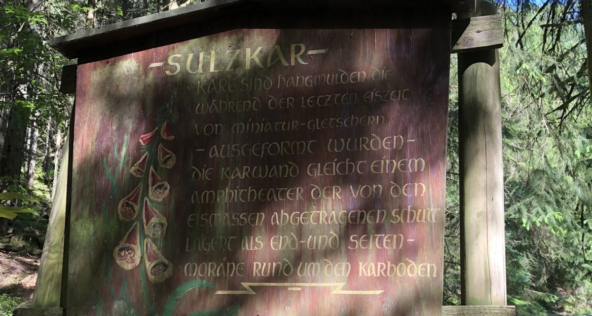 Ein Holzschild im Wald mit der Aufschrift 'Sulzkar' und Informationen über die geologische Formation. Umgeben von Bäumen und Sonnenlicht., © Nördlicher Schwarzwald Ein Holzschild im Wald mit der Aufschrift 'Sulzkar' und Informationen über die geologische Formation. Umgeben von Bäumen und Sonnenlicht., © Nördlicher Schwarzwald