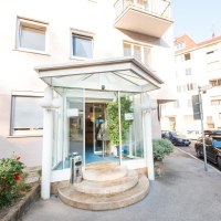 Hoteleingang mit Glas&uuml;berdachung und runden Stufen, umgeben von Autos und Pflanzen. Geb&auml;ude mit mehreren Fenstern im Hintergrund., &copy; ARNOTEL GmbH