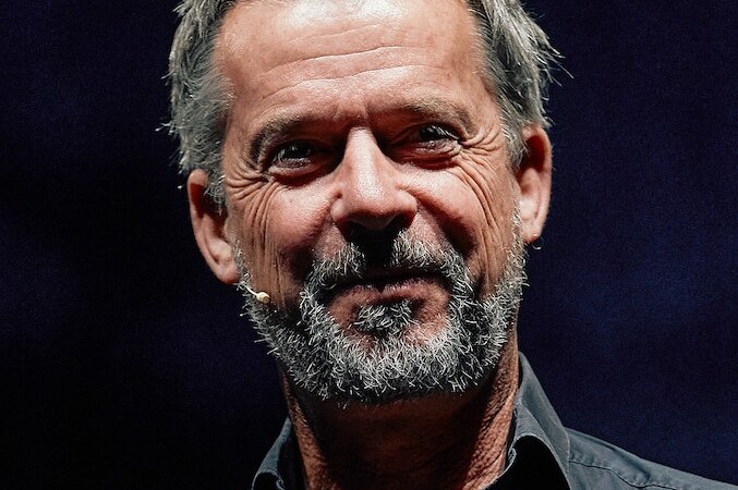 Ein Mann mit grauem Bart und Mikrofon l&auml;chelt vor einem dunklen Hintergrund. Er tr&auml;gt ein dunkles Hemd., &copy; Stadtverwaltung Remseck am Neckar