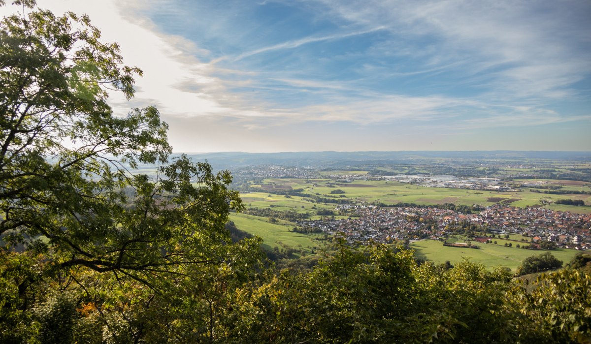 Blick vom Aussichtspunkt Hoher Fels auf eine weite Landschaft mit Feldern, einem Dorf und bewölktem Himmel. Bäume rahmen das Bild ein., © Foto Thomas Zehnder Blick vom Aussichtspunkt Hoher Fels auf eine weite Landschaft mit Feldern, einem Dorf und bewölktem Himmel. Bäume rahmen das Bild ein., © Foto Thomas Zehnder