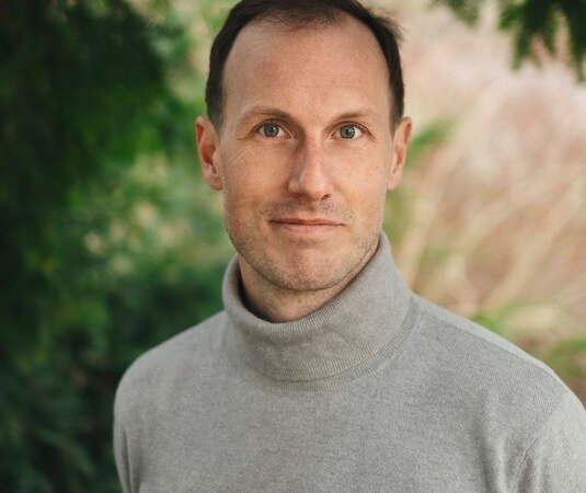 Ein Mann in einem grauen Rollkragenpullover steht vor einem unscharfen, grünen Hintergrund und schaut in die Kamera., © Osiander Vertriebsgesellschaft mbH & Co. KG Ein Mann in einem grauen Rollkragenpullover steht vor einem unscharfen, grünen Hintergrund und schaut in die Kamera., © Osiander Vertriebsgesellschaft mbH & Co. KG