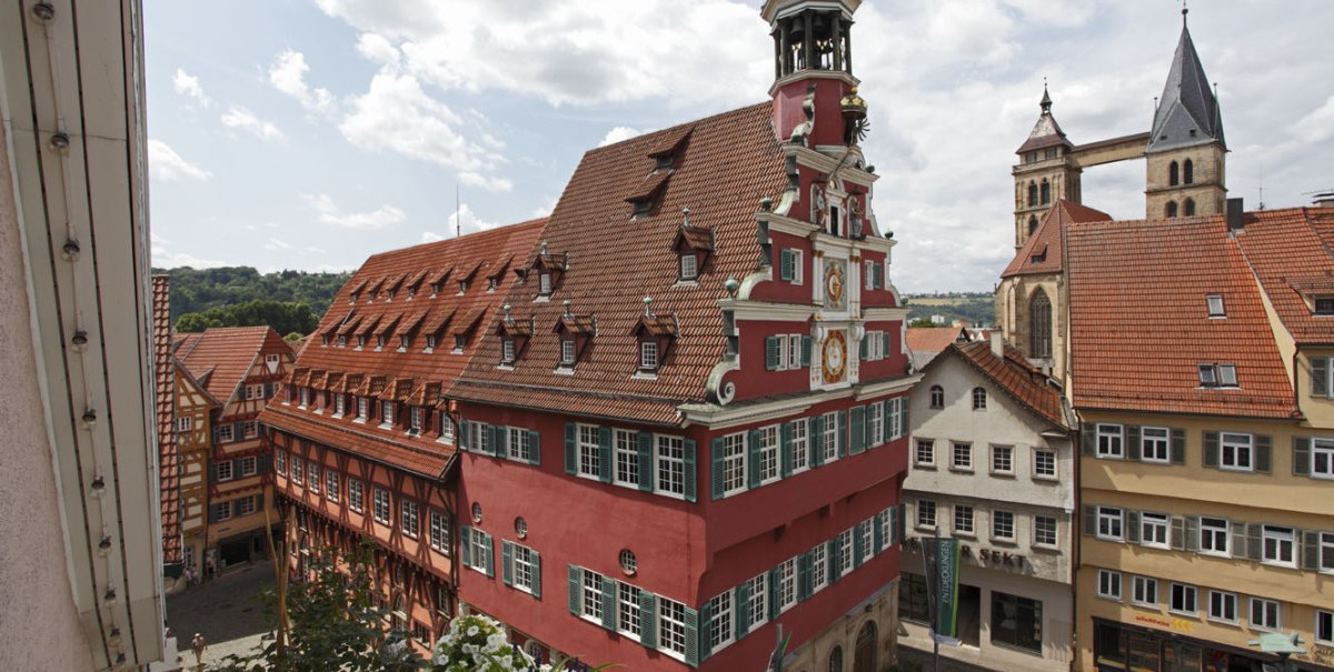 Das Alte Rathaus in Esslingen mit rotem Fachwerk und Turm, umgeben von historischen Gebäuden und blühenden Blumen im Vordergrund., © Esslinger Stadtmarketing & Tourismus GmbH