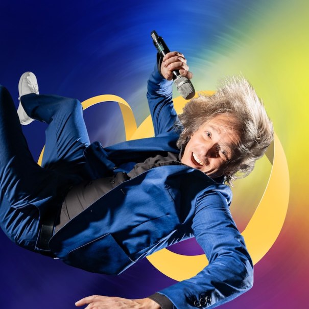 Ein Mann in blauem Anzug schwebt mit Mikrofon vor buntem Hintergrund. Dynamische Pose und lebendige Farben., © Stadtverwaltung Vaihingen an der Enz Ein Mann in blauem Anzug schwebt mit Mikrofon vor buntem Hintergrund. Dynamische Pose und lebendige Farben., © Stadtverwaltung Vaihingen an der Enz