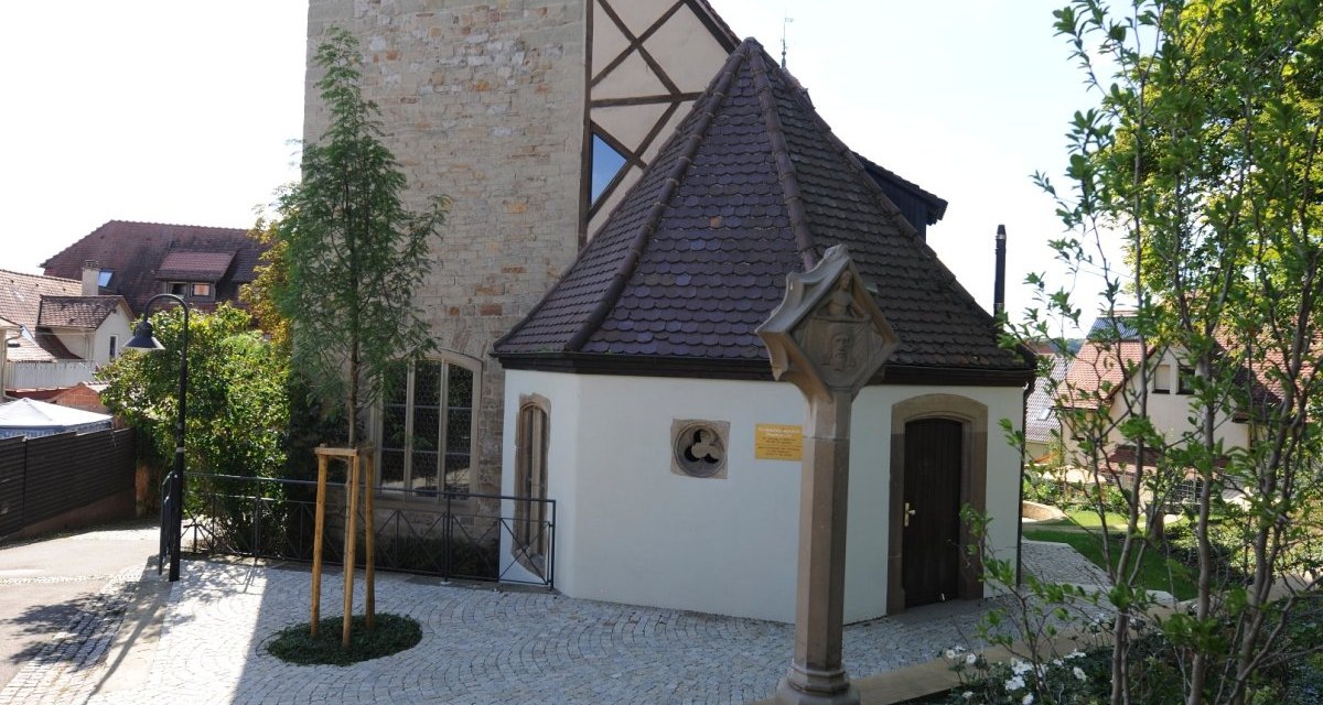 Eingang der Peterskirche in Vaihingen an der Enz, mit Fachwerkturm, gepflastertem Weg und blühendem Garten im Vordergrund., © Land der 1000 Hügel - Kraichgau-Stromberg Eingang der Peterskirche in Vaihingen an der Enz, mit Fachwerkturm, gepflastertem Weg und blühendem Garten im Vordergrund., © Land der 1000 Hügel - Kraichgau-Stromberg