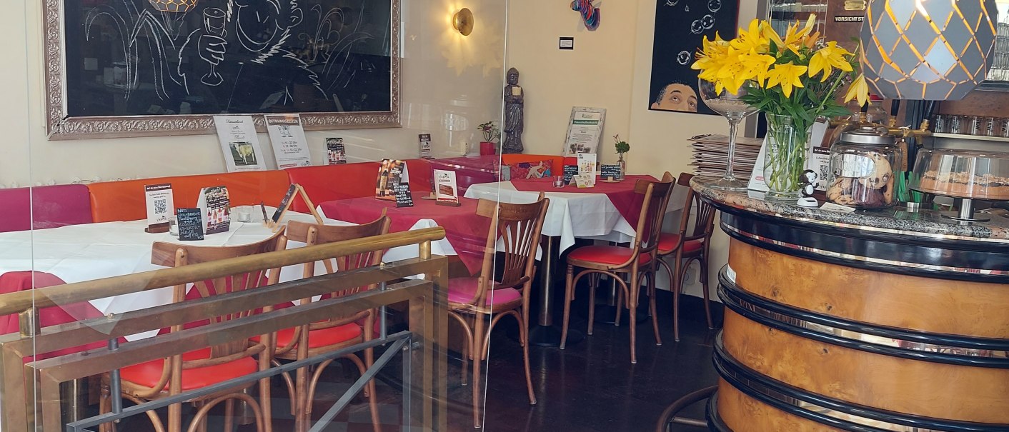 Ein gemütliches Restaurant mit Tafeln, gelben Blumen und gedeckten Tischen. Der Schriftzug 'V Bandits' ist auf einer Tafel zu sehen., © Lisa Bakavos V-Bandits Ein gemütliches Restaurant mit Tafeln, gelben Blumen und gedeckten Tischen. Der Schriftzug 'V Bandits' ist auf einer Tafel zu sehen., © Lisa Bakavos V-Bandits